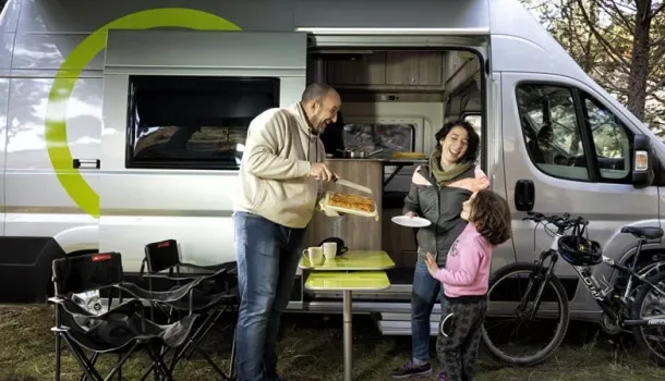Imagen de una famlia merendando en el exterior de la camper con productos de camping incluidos