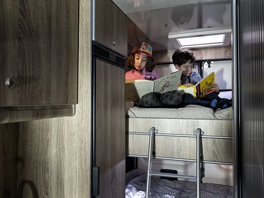 Imagen de unos niños en la cama de matrimonio de una furgoneta camperizada 